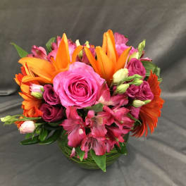 Pink and orange mixed flower arrangement in a round glass vase