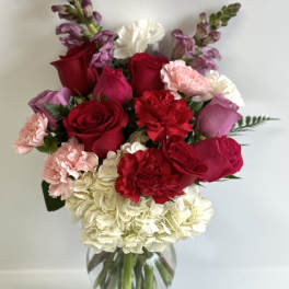 Bouquet of red roses, pink carnations, and white hydrangea in a glass vase
