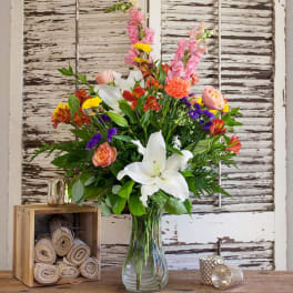Mixed bouquet with white lilies, pink snapdragons, and orange blooms in a glass vase