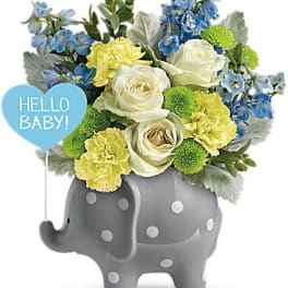 Baby-themed bouquet of white roses and yellow flowers in a gray polka-dot elephant container with blue accents