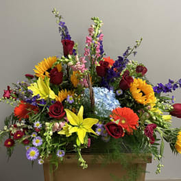Large mixed flower arrangement with sunflowers, roses, and lilies in a wooden container