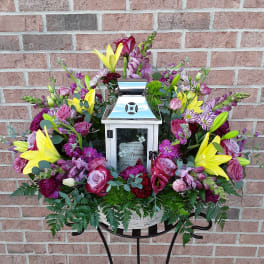 Floral funeral arrangement around a silver lantern in a basket