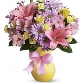 Bouquet of pink and lavender flowers in a yellow vase with a pink ribbon
