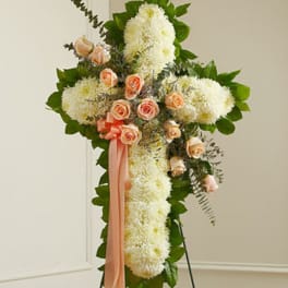 Standing floral cross with white blooms, peach roses, and pink ribbon