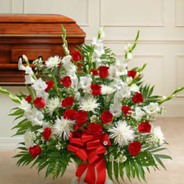 Red and white funeral spray with roses and lilies beside a casket