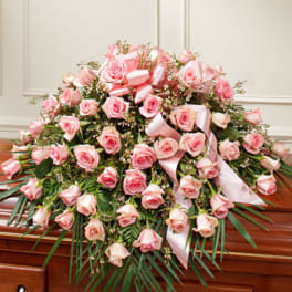 Large pink rose casket spray with ribbon on a wooden casket