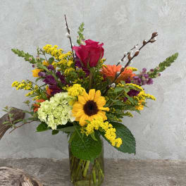 Colorful mixed flower arrangement in a glass vase with a sunflower and pink rose
