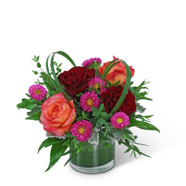 Orange and red roses with pink daisies in a glass vase