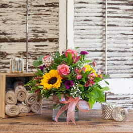 Mixed bouquet with a sunflower, pink roses, and purple blooms in a glass vase