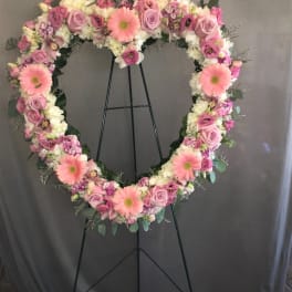 Heart-shaped floral wreath on a black stand with pink and white flowers