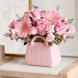 Pink roses, gerbera daisies, and carnations in a pink purse-shaped ceramic vase
