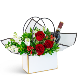 Red roses and white flowers in a gift box with a wine bottle