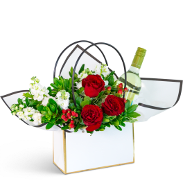 Red roses and white flowers in a gift bag with a wine bottle