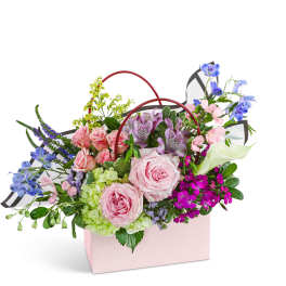 Mixed flower arrangement in a pink gift bag with red handles