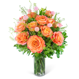 Orange roses in a clear glass vase with pink accent flowers