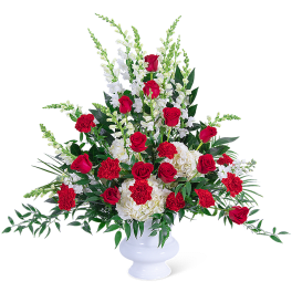 Red roses and white flowers arranged in a white urn vase