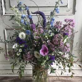 Mixed bouquet of blue, pink, and white flowers in a clear glass vase