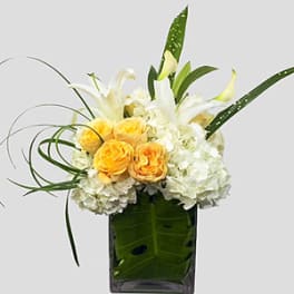 Yellow roses and white lilies in a tall glass vase