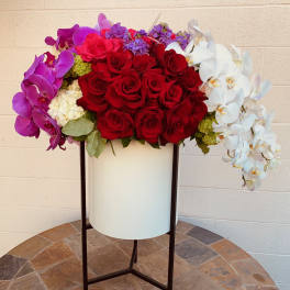 Large floral arrangement of red roses, purple orchids, and white orchids in a tall stand
