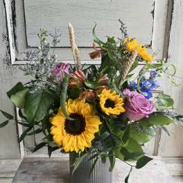 Mixed bouquet with sunflowers, pink roses, and blue flowers in a metal vase
