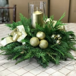 Green holiday centerpiece with gold ornaments and a glass candle holder