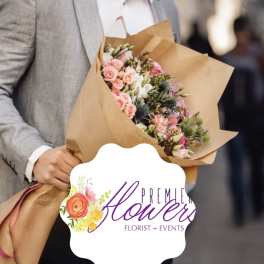 Handheld bouquet of pink and white flowers wrapped in brown paper