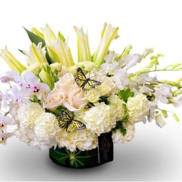 White and pale pink floral arrangement in a black vase with butterfly accents
