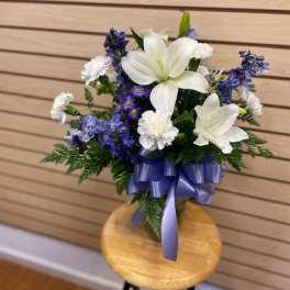 White lilies and blue flowers in a vase with a purple ribbon