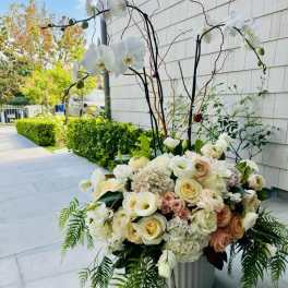 Large white floral arrangement with orchids and roses in a metal container