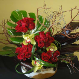 Red roses and yellow orchids arranged in a low container with branches