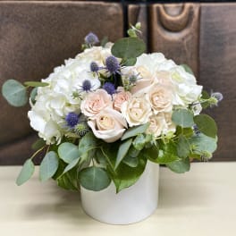 White and blush roses with purple thistle in a white vase
