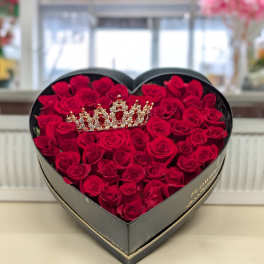 Heart-shaped black box filled with red roses and a jeweled crown ornament on top