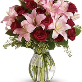 Arrangement of red roses and pink lilies in a clear glass vase with water