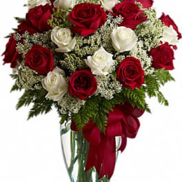 Arrangement of red and white roses with white filler flowers in a clear vase with a red ribbon bow
