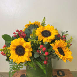Sunflower arrangement in a glass vase with red berry accents