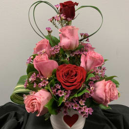 Pink and red roses in a white heart vase with a heart-shaped wire accent