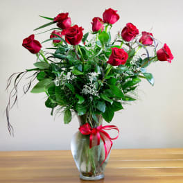 Red roses arranged in a clear glass vase with a red ribbon