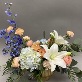 Mixed bouquet with white lilies, blue delphinium, and peach roses in a vase