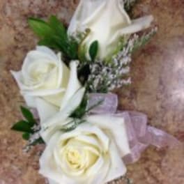 White rose corsage with small purple filler flowers and a lavender ribbon