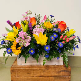 Bright mixed bouquet with sunflowers, roses, and blue daisies in a wooden box