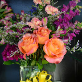 Orange roses and purple flowers in a glass vase with a yellow ribbon