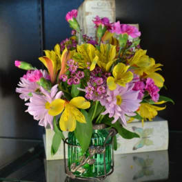 Colorful bouquet of pink, yellow, and lavender flowers in a green glass vase