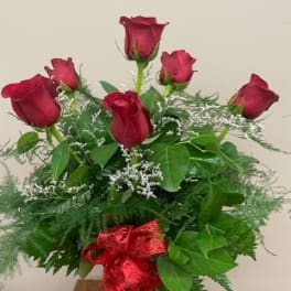 Red roses arranged in a glass vase with a red ribbon