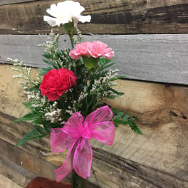 Small bouquet of carnations in a clear glass vase with a pink ribbon