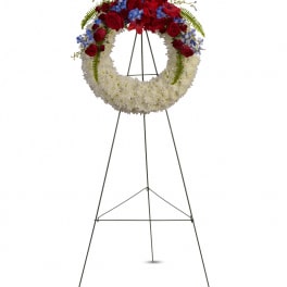 Standing floral wreath with red roses, white flowers, and blue accents on a metal easel