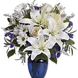 White lilies and daisies arranged in a blue glass vase
