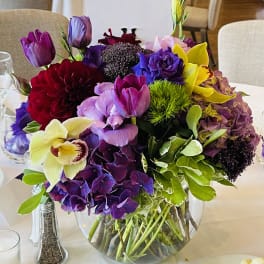 Mixed bouquet of purple, pink, yellow, and red flowers in a glass vase