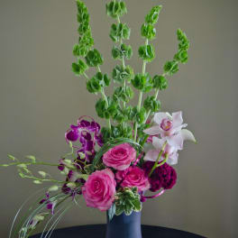 Tall bouquet with pink roses, purple orchids, and white orchids in a purple vase