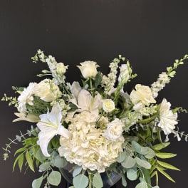 White floral arrangement in a clear vase with lilies, roses, and daisies