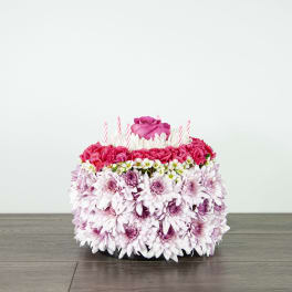 Round floral cake with pink roses, carnations, and candles